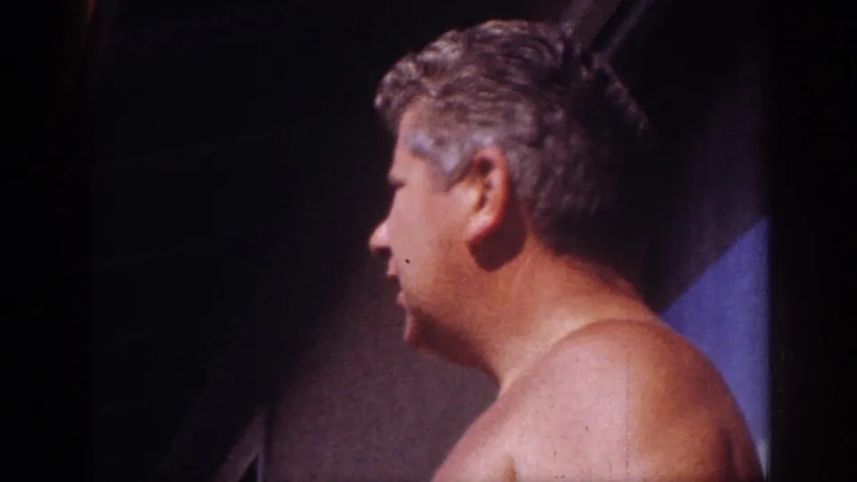 Side view of a shirtless adult man near a shaded exterior wall in Blainsport, Pennsylvania, 1962 home-movie footage.