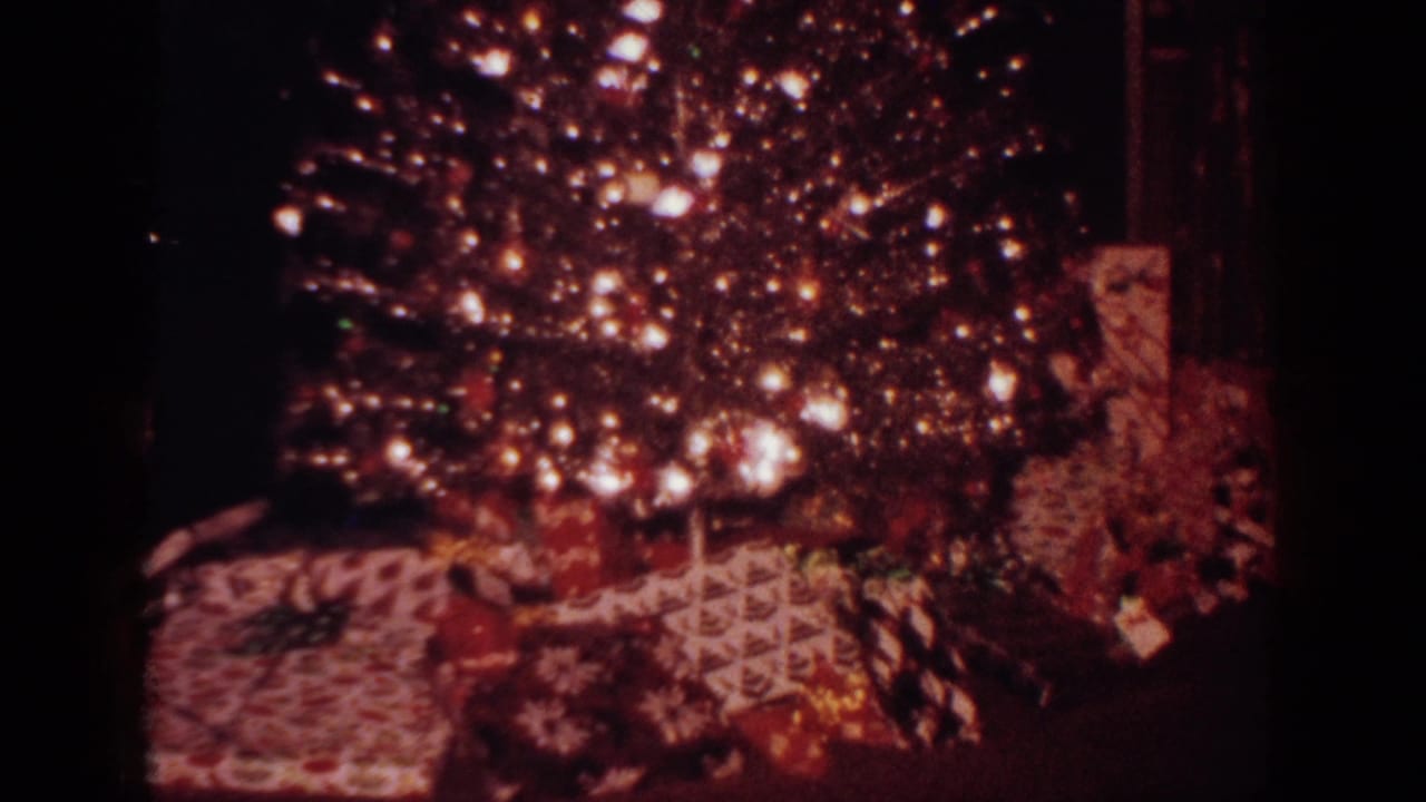 Home-movie frame from the 1962 clip showing a lit Christmas tree and wrapped presents in a dark interior.