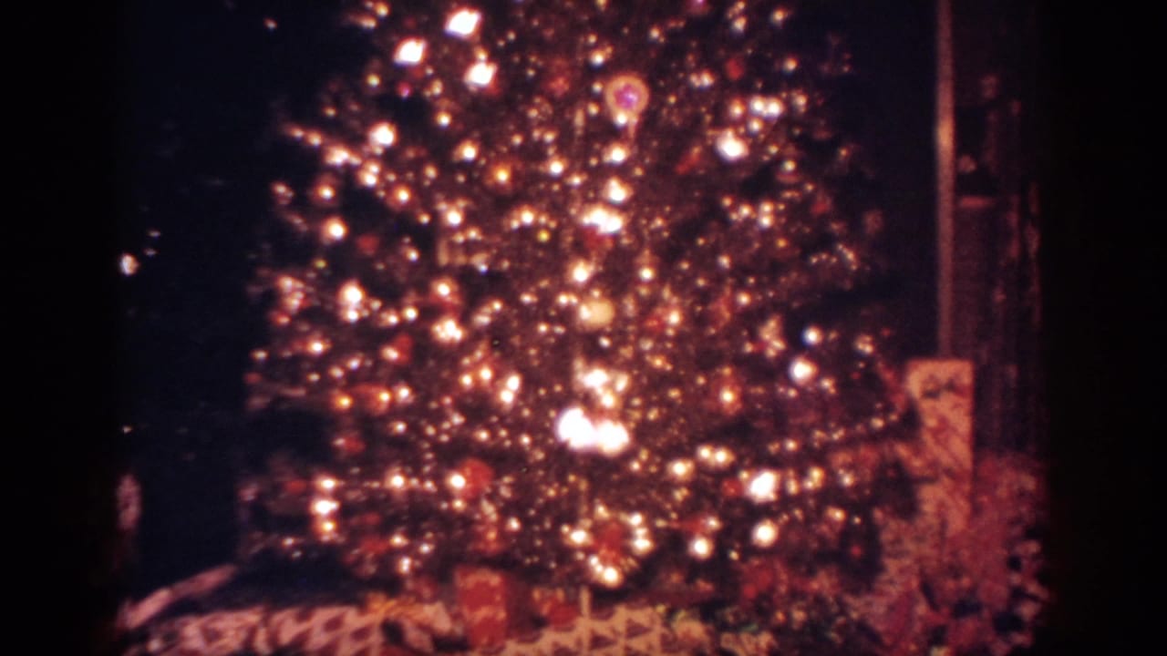 1962 Blainsport home-movie frame of a decorated Christmas tree with bright lights, ornaments, and wrapped gifts below.
