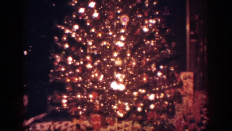 1962 Blainsport home-movie frame of a decorated Christmas tree with bright lights, ornaments, and wrapped gifts below.