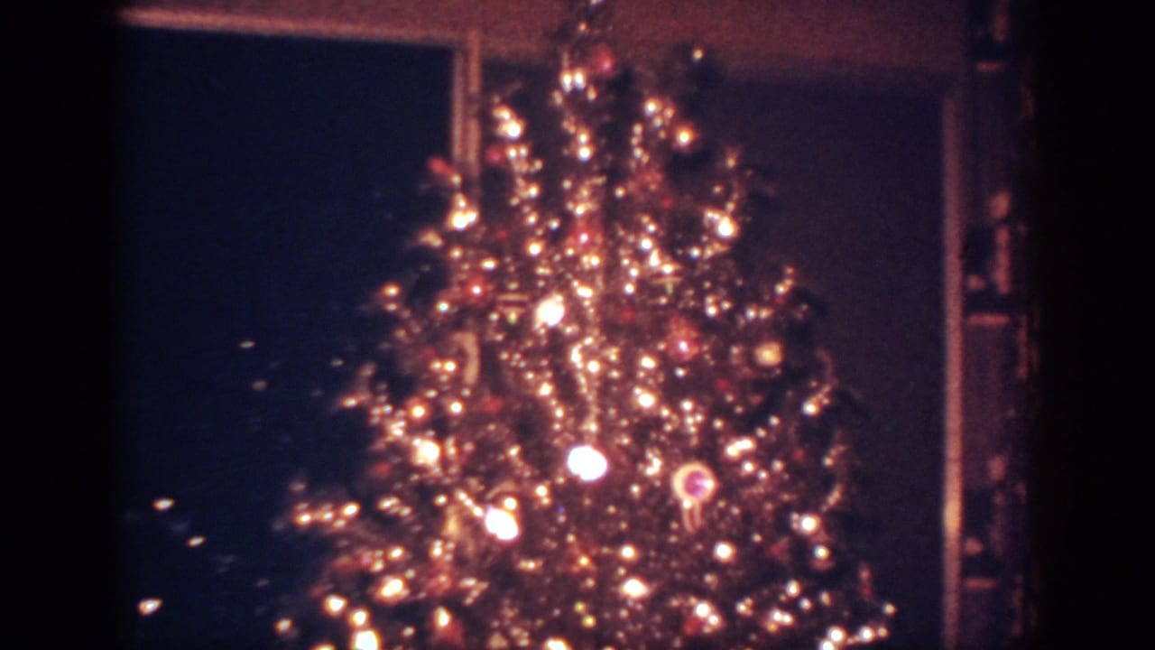 1962 Blainsport home-movie frame showing a lit Christmas tree with ornaments and tinsel in a dim room.