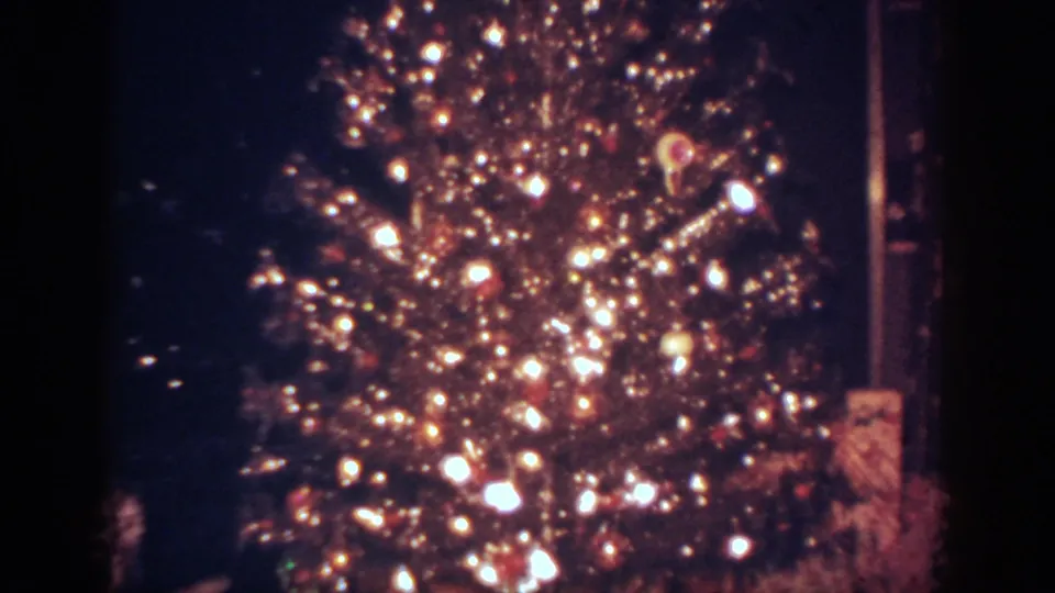 1962 Blainsport frame showing the lit tree near a small wrapped item at the base in a dark room.