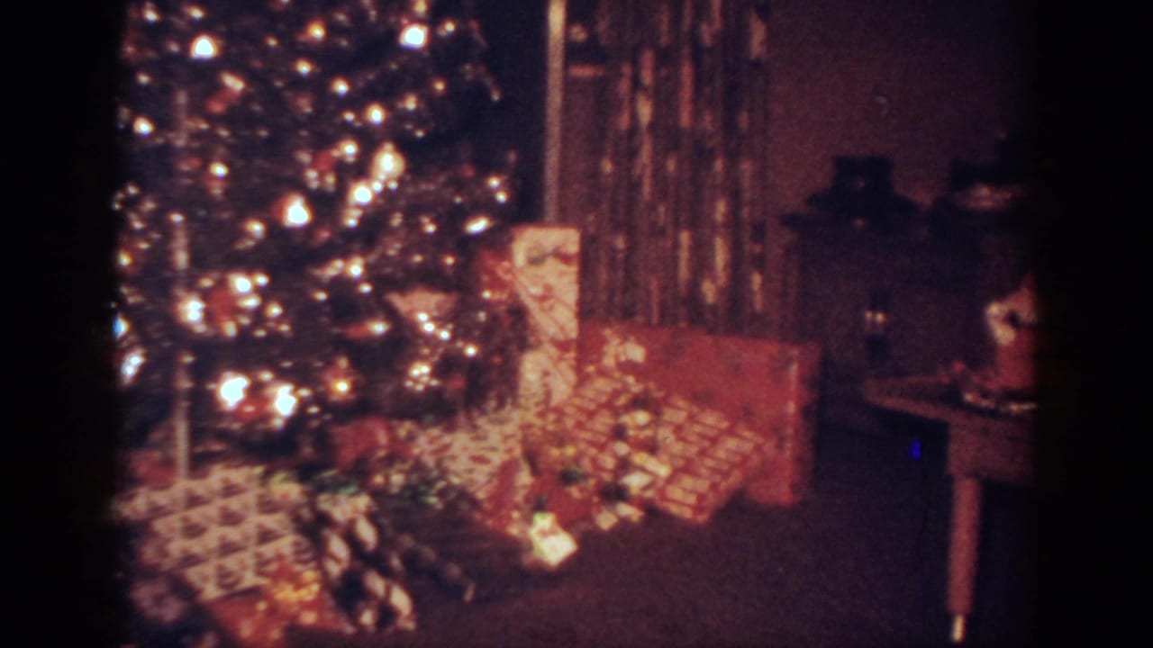 1962 Blainsport home-movie frame showing a lit Christmas tree beside wrapped presents in a private living room.