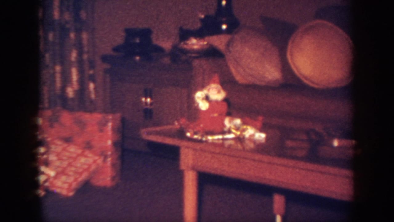 1962 Blainsport home-movie frame showing a small Santa figurine, tinsel, and gifts on a wooden table.