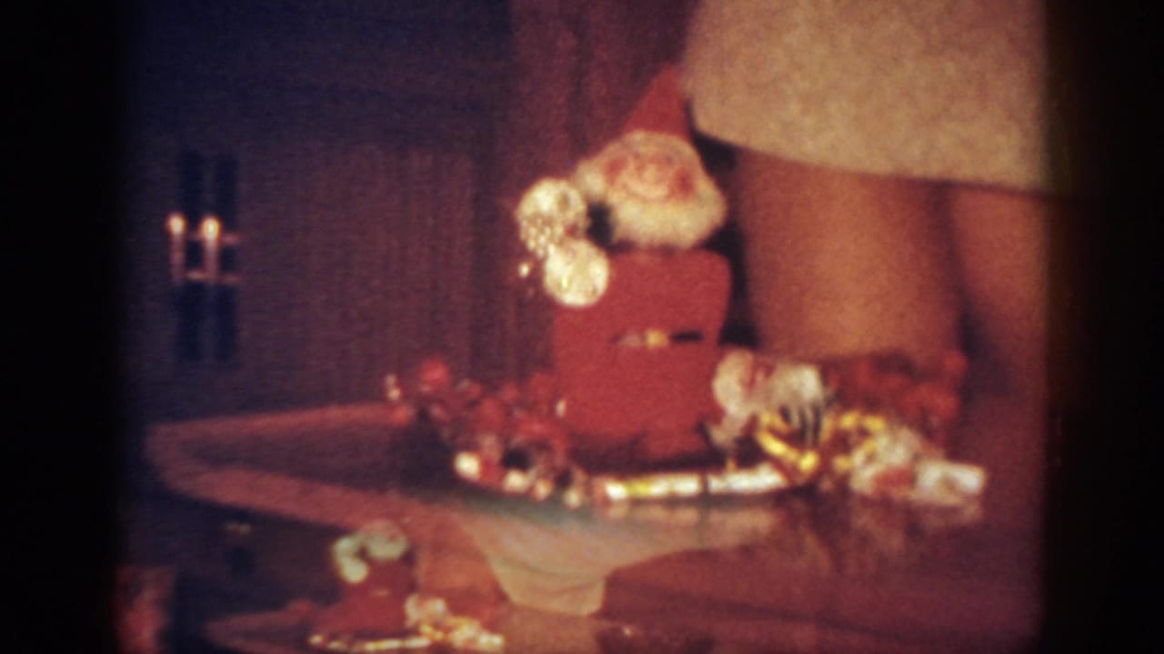 1962 Blainsport home-movie frame showing a tabletop Santa decoration, holiday trim, and the lower half of a woman in a white dress.