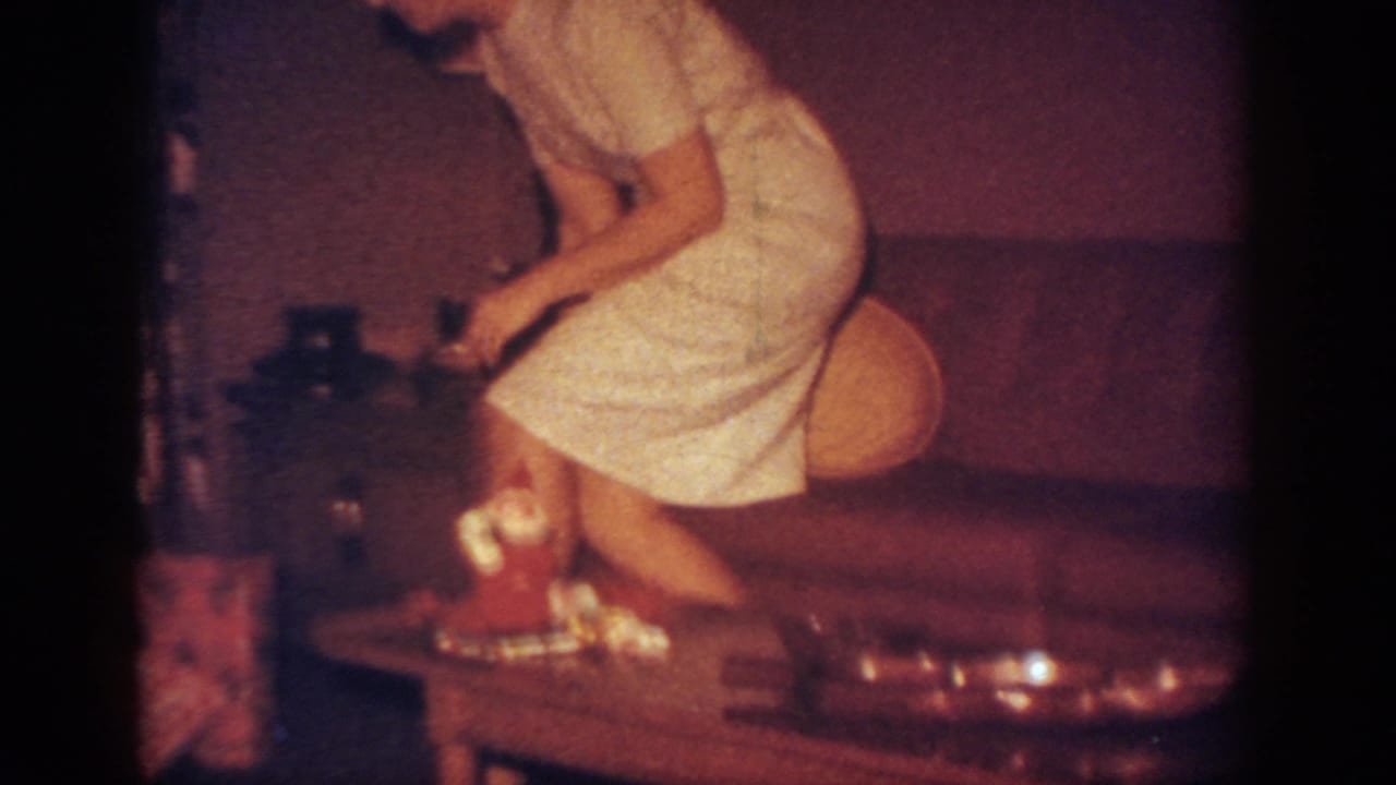 Woman rises or leans over a coffee table with presents and a small Santa decoration in a living room.