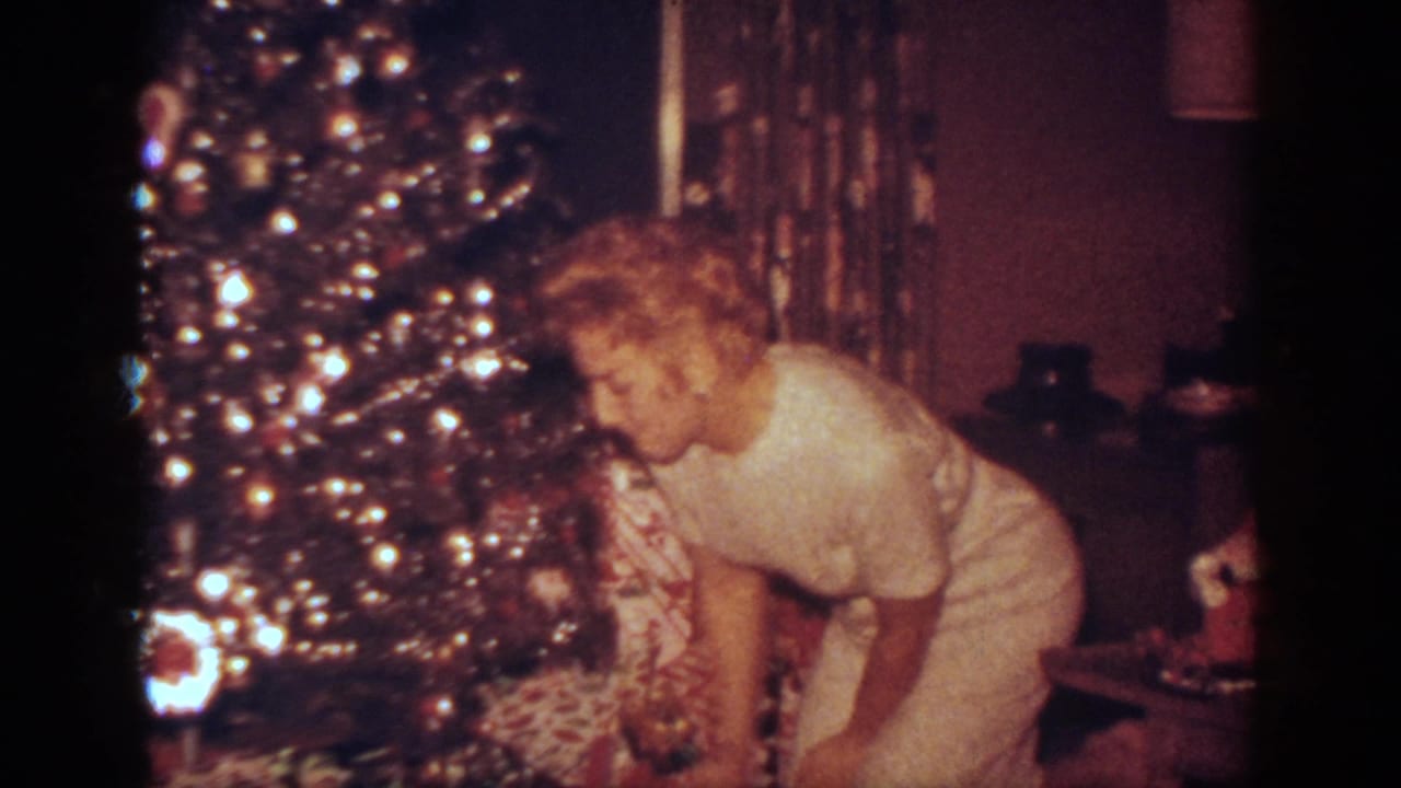 In a 1962 Blainsport home interior, a woman in a white dress leans toward wrapped presents beneath a bright Christmas tree.