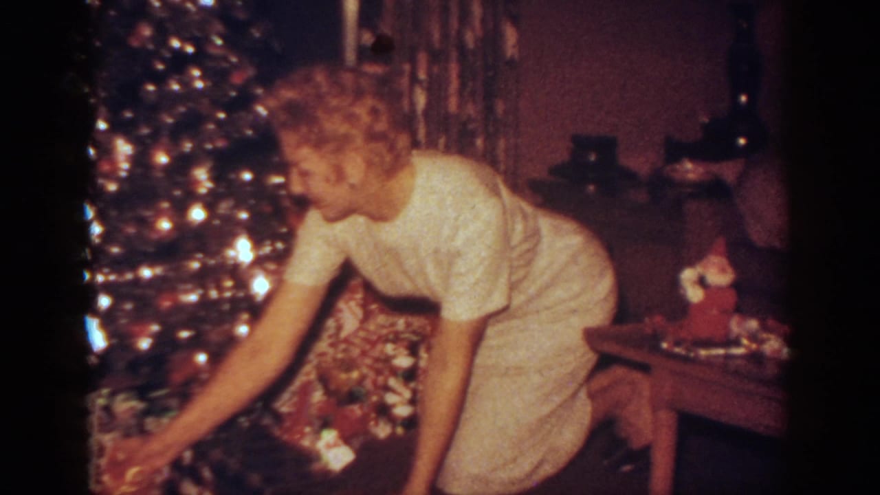 Woman bends toward wrapped presents beneath a lit Christmas tree in a living room.