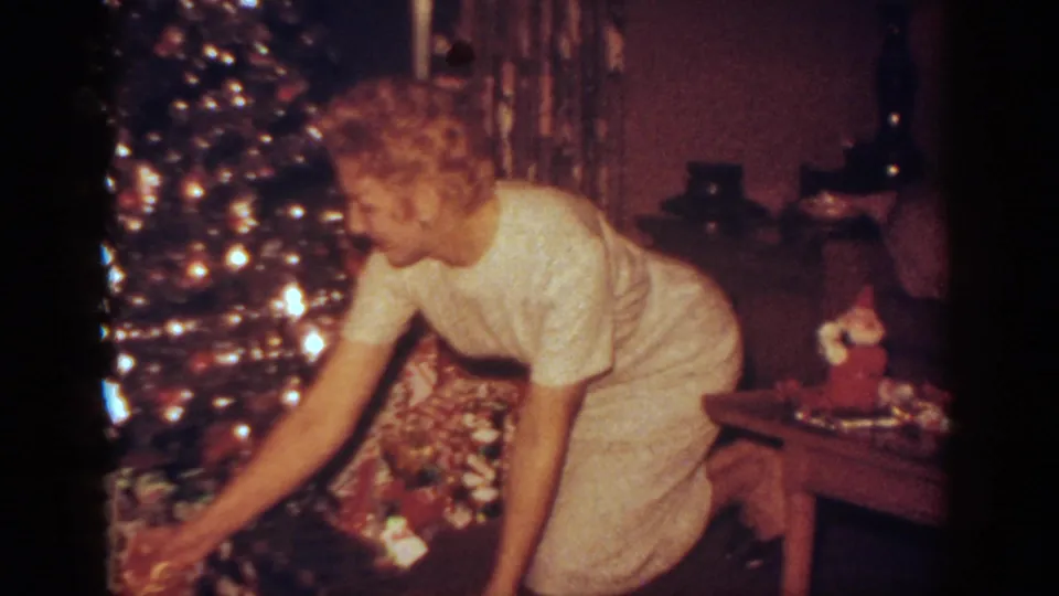The woman leans toward gifts under the Christmas tree in the documented 1962 Blainsport, Pennsylvania home-movie scene.