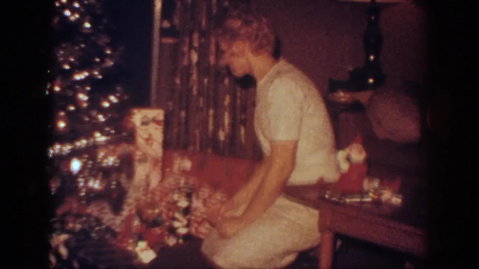 A side view shows the woman kneeling by the lit tree, arranging Christmas gifts in the private living-room setting.