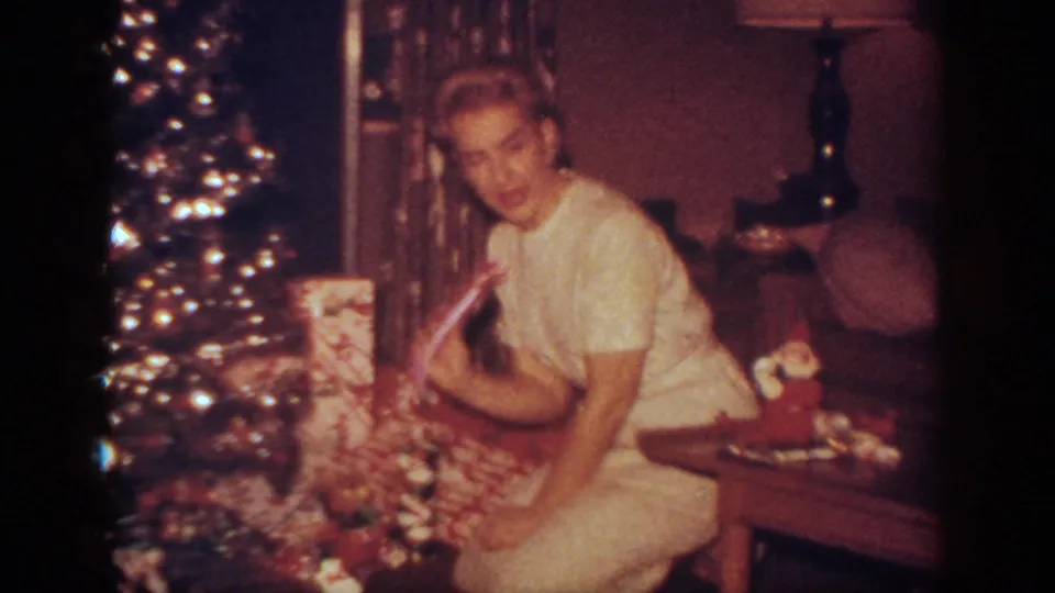 The woman turns toward the camera near the Christmas tree and wrapped gifts in the 1962 Blainsport home-movie interior.