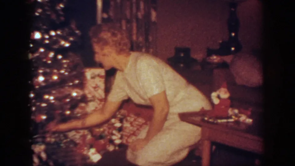 A woman kneels and reaches toward gifts at the foot of the Christmas tree in this 1962 Pennsylvania home-movie frame.