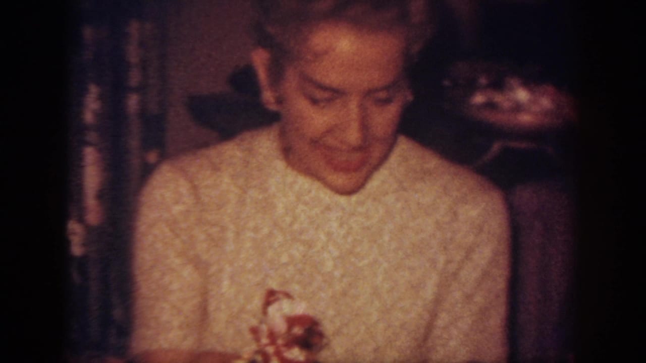 Woman in a light sweater looks down while holding a small object near holiday decorations.