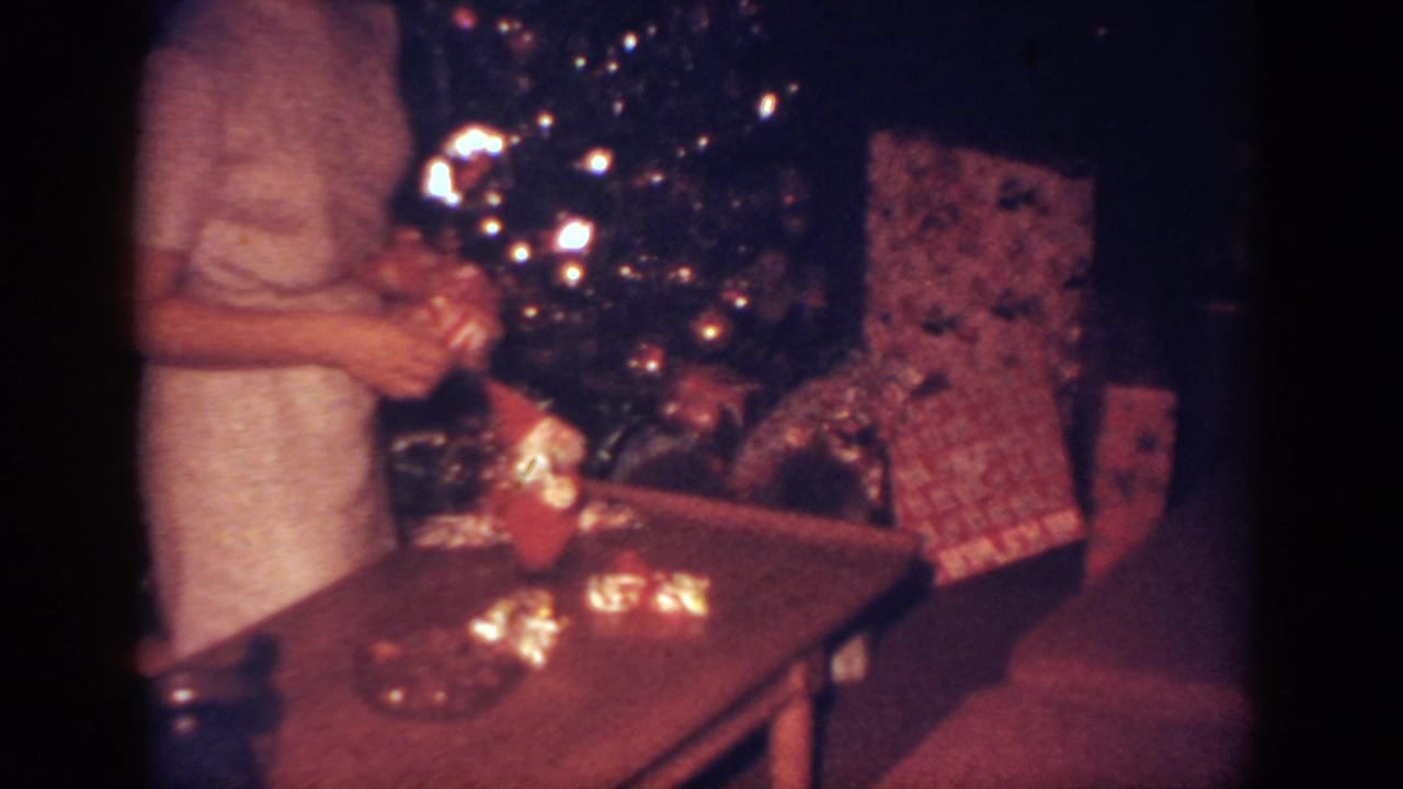 The woman appears to handle a decoration or gift beside the lit Christmas tree in the Blainsport living room.