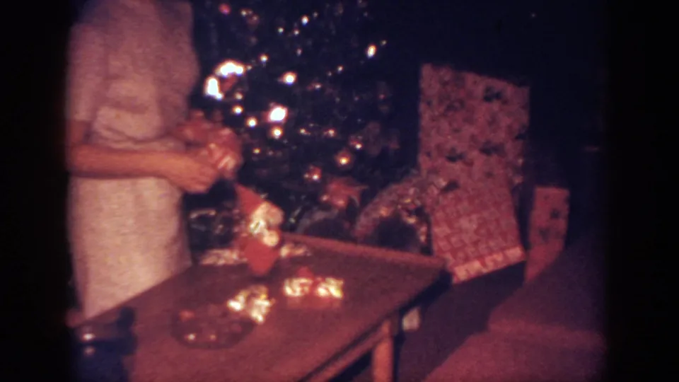 The woman appears to handle a decoration or gift beside the lit Christmas tree in the Blainsport living room.