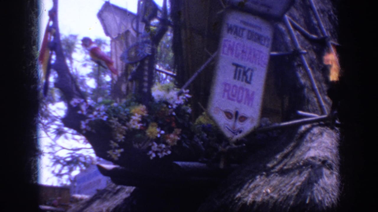 1962 Anaheim Disneyland frame of the Enchanted Tiki Room sign with flowers, thatch, branchwork, and a small flame torch at the right edge.