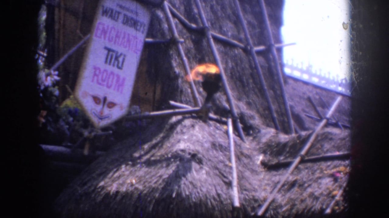 1962 Anaheim home-movie frame showing the Enchanted Tiki Room exterior sign, thatched roof, bamboo supports, and a burning torch.