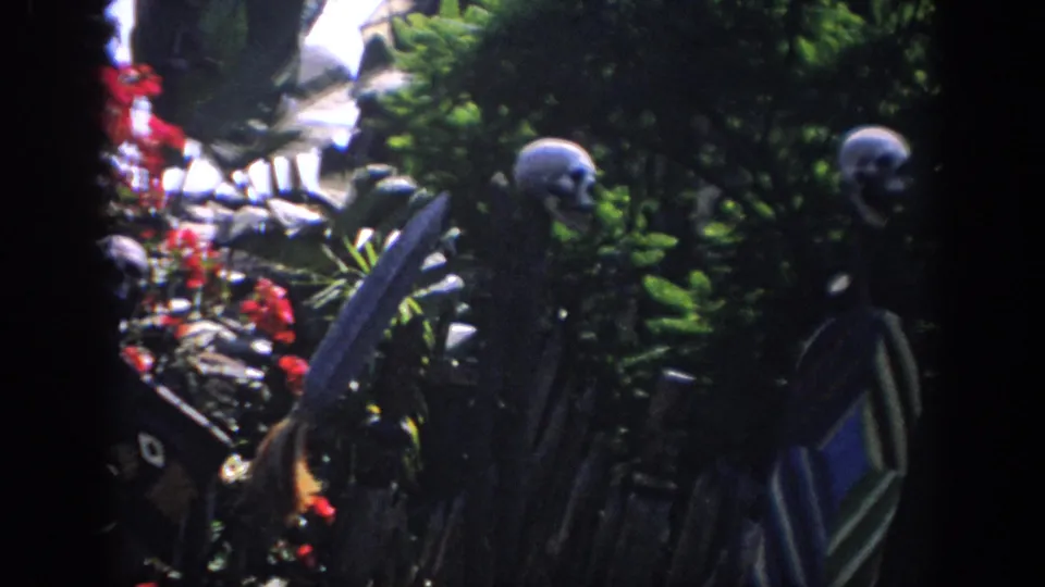 1962 Anaheim home-movie frame of skeleton figures in a planted garden scene, with saturated foliage and strong shadow at the sides.