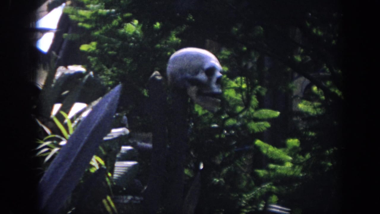 A skull prop on a stake stands beside broad leaves and dense greenery.