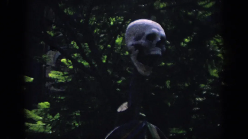 1962 Anaheim 8mm frame with a large skull prop set deep in shadowed jungle-style foliage.