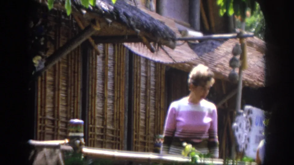 1962 Anaheim 8mm frame with an adult woman near a thatched bamboo-style hut and pale decorative object.