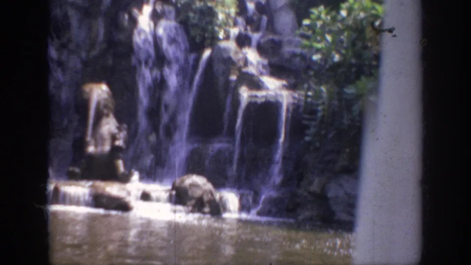 1962 Anaheim 8mm frame showing water falling over layered rockwork into a calm lagoon.