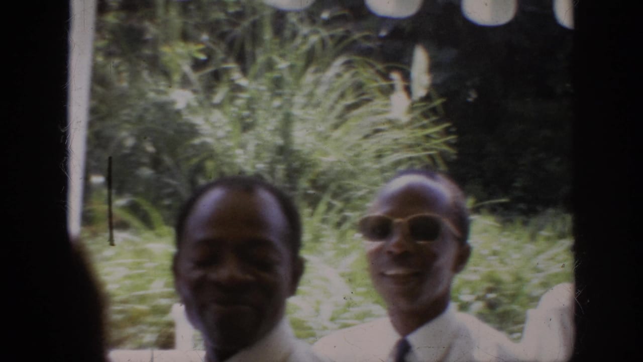 1962 Anaheim 8mm frame showing two Black adult men in dress shirts and ties smiling near lush outdoor foliage.