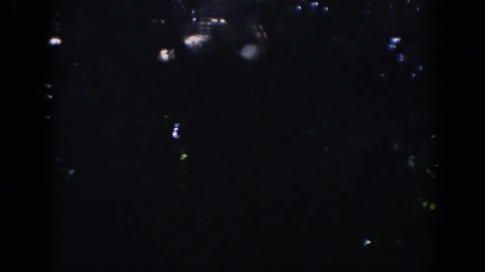 Dark 8mm frame from the Anaheim home-movie clip, with scattered highlights and heavy shadow before the ride view appears.