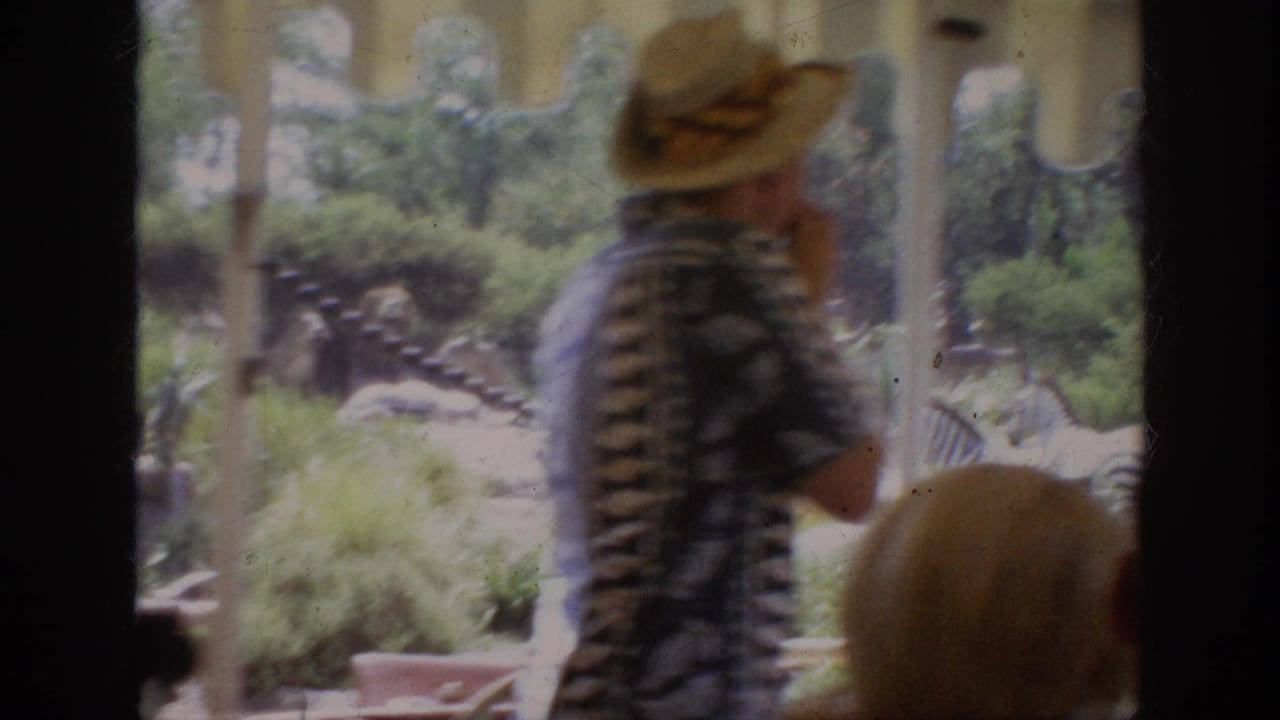 1962 Anaheim home-movie frame showing a man in a straw hat inside an open tram, with zoo animals visible beyond the window.