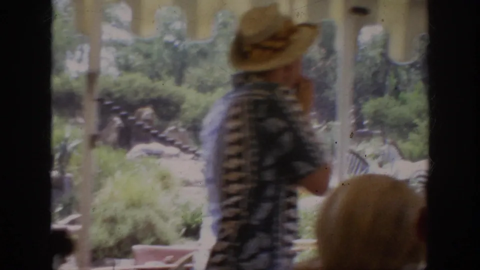 1962 Anaheim home-movie frame showing a man in a straw hat inside an open tram, with zoo animals visible beyond the window.