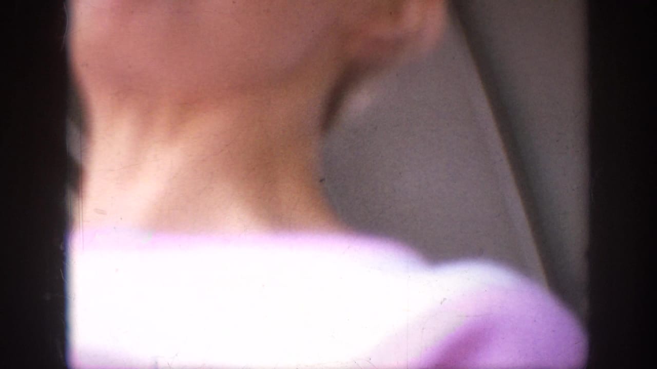 Soft-focus 1962 Anaheim home-movie frame with a close foreground shoulder and neck partially obscuring the outdoor setting.