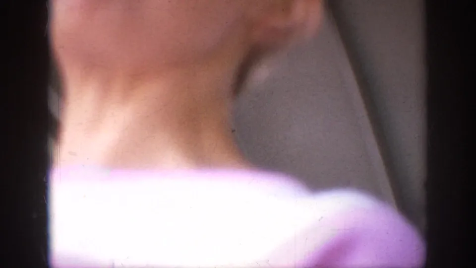 Soft-focus 1962 Anaheim home-movie frame with a close foreground shoulder and neck partially obscuring the outdoor setting.
