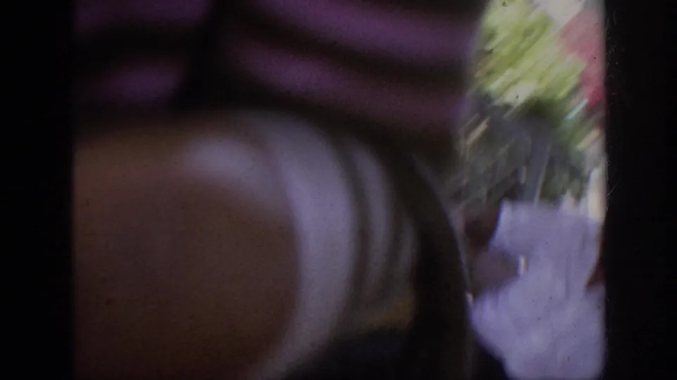 Motion-blurred 1962 Anaheim home-movie frame with a foreground figure, flowers, and fragments of an outdoor pedestrian area.