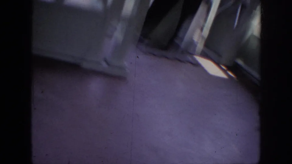 Tilted 1962 Anaheim home-movie frame showing pavement, a storefront or doorway, and passing pedestrians at the edge of view.