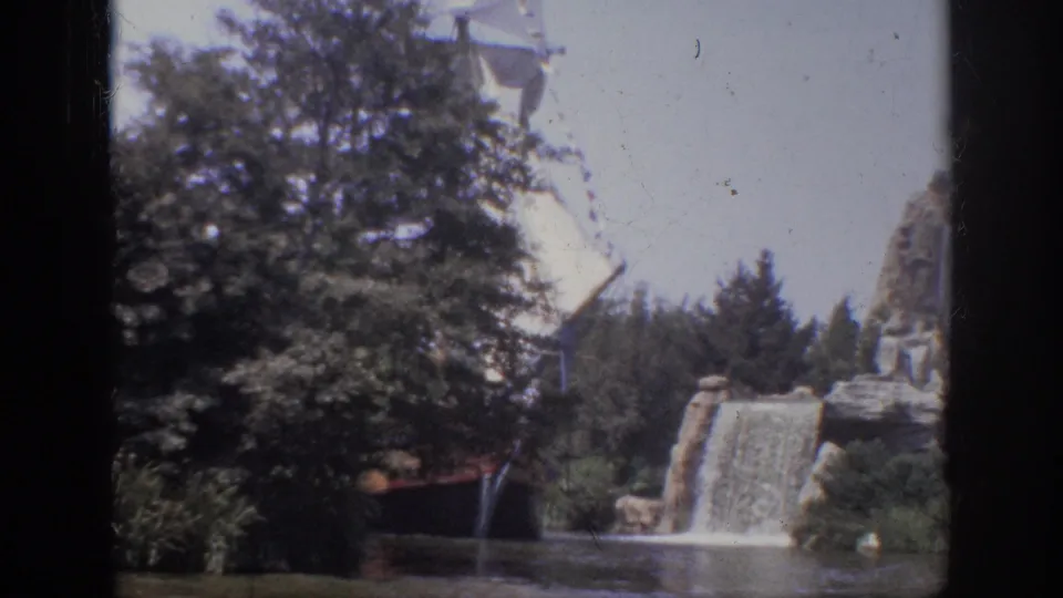 1962 Anaheim 8mm frame showing the white sail more prominently above trees, with a rock waterfall and calm lagoon below.