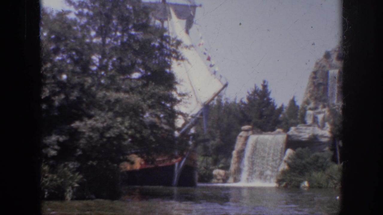1962 Anaheim home-movie frame showing a pirate-style sailing ship near a cascading waterfall, with trees, rocks, and river water in view.