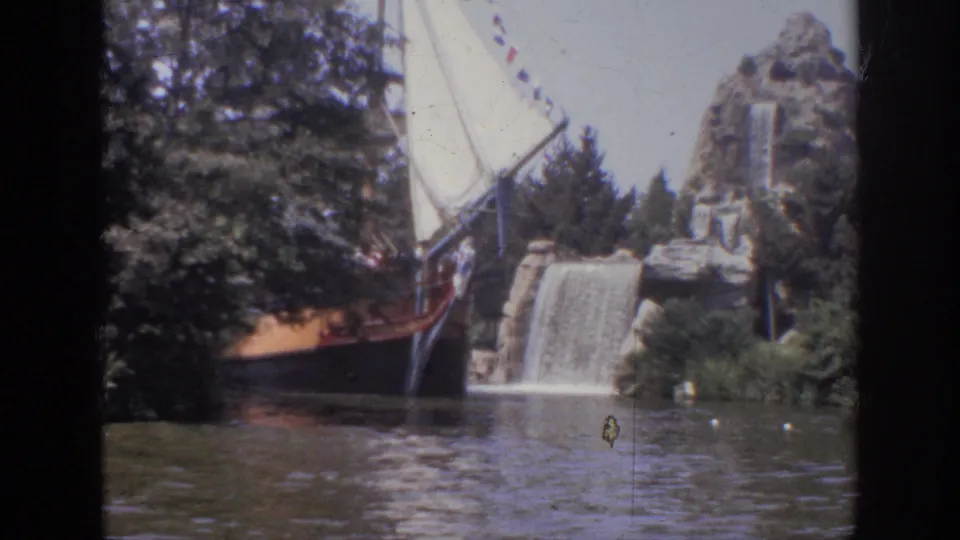 1962 Anaheim frame showing the themed ship near a small waterfall, surrounded by trees, shrubs, artificial rocks, and visible 8mm frame borders.