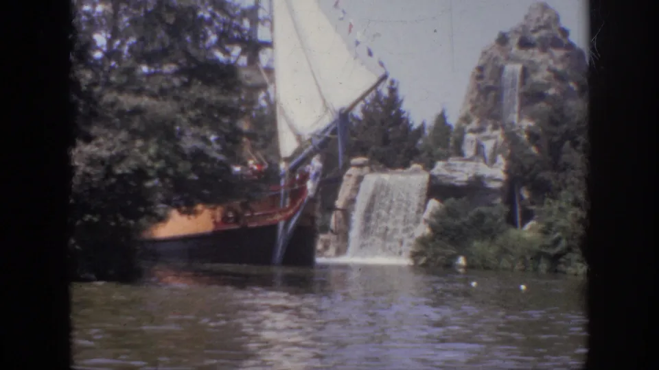 1962 Anaheim 8mm frame showing a themed wooden boat with white sails near an artificial waterfall and lagoon.