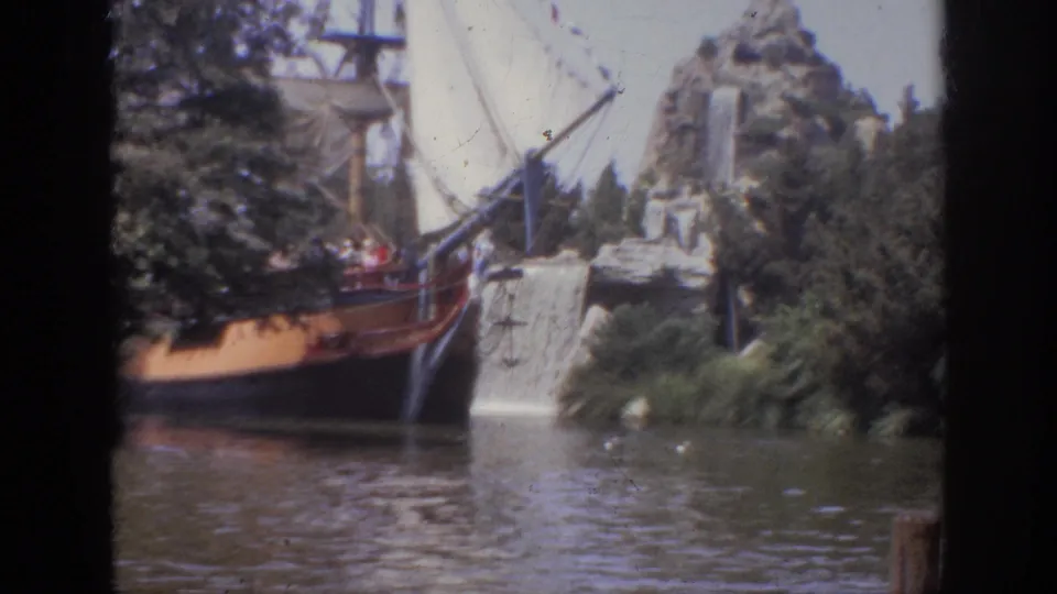 1962 Anaheim home-movie frame of a sailboat-themed ride beside a cascading waterfall, trees, and artificial rocky scenery.