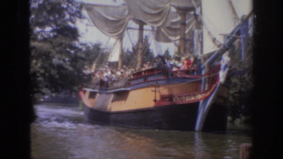 1962 Anaheim vacation footage frame with a red-trimmed sailing-ship ride carrying visitors beside foliage and water.