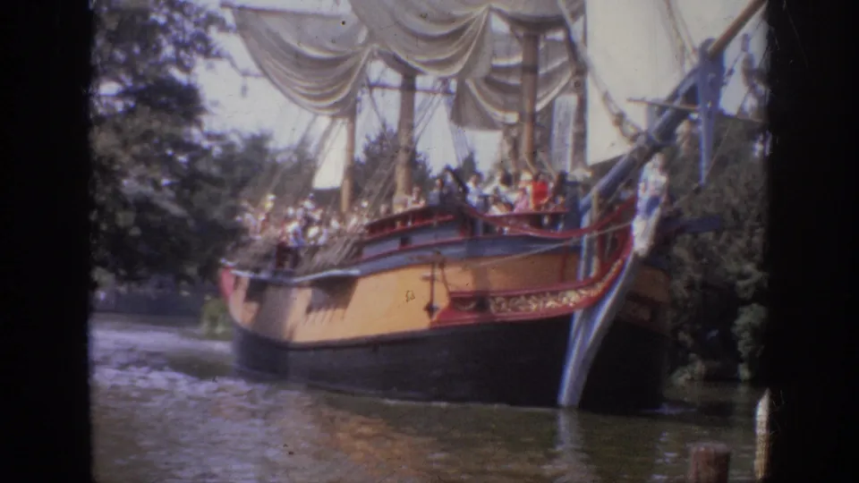 Soft 8mm frame from 1962 Disneyland showing a replica sailing ship near the camera, with visitors aboard and water below.