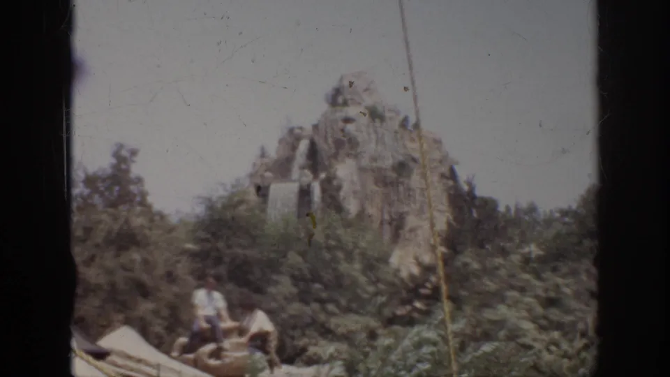 1962 Anaheim frame showing workers near artificial rockwork, dense plantings, and a small waterfall-like feature.
