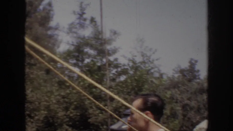 1962 Anaheim visitor footage with a man in profile in the foreground, ropes crossing the frame, and trees behind him.