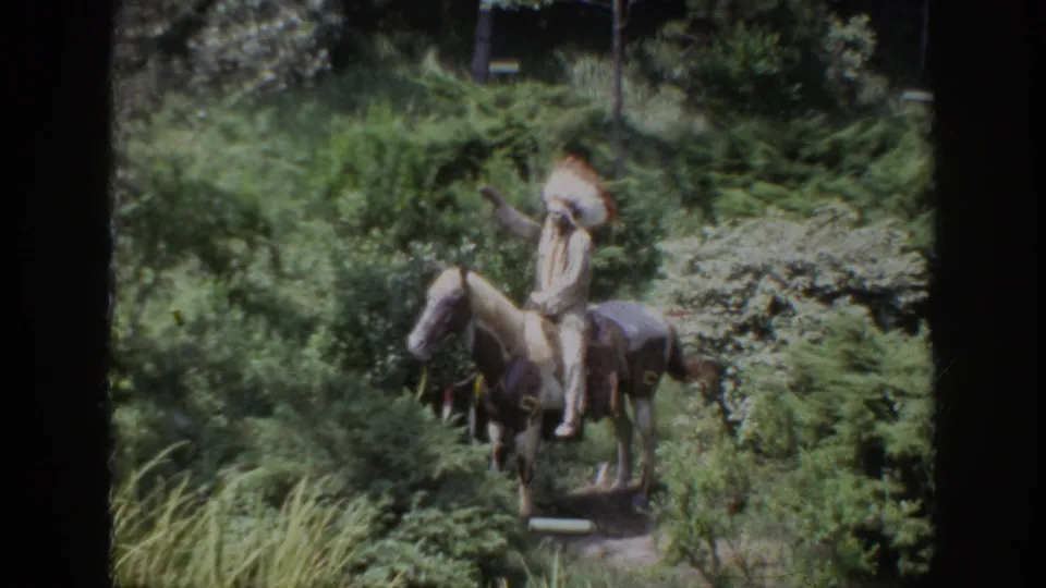 1962 Anaheim home-movie view of a Native American figure on horseback, partly obscured by shrubs and film softness.