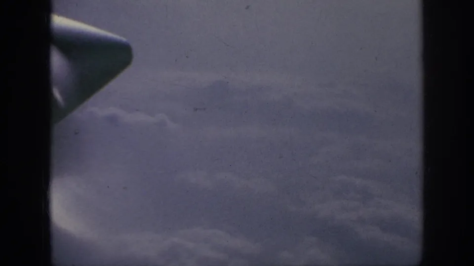 1962 passenger-window view with an aircraft wingtip near the frame edge and clouds stretching into the distance.