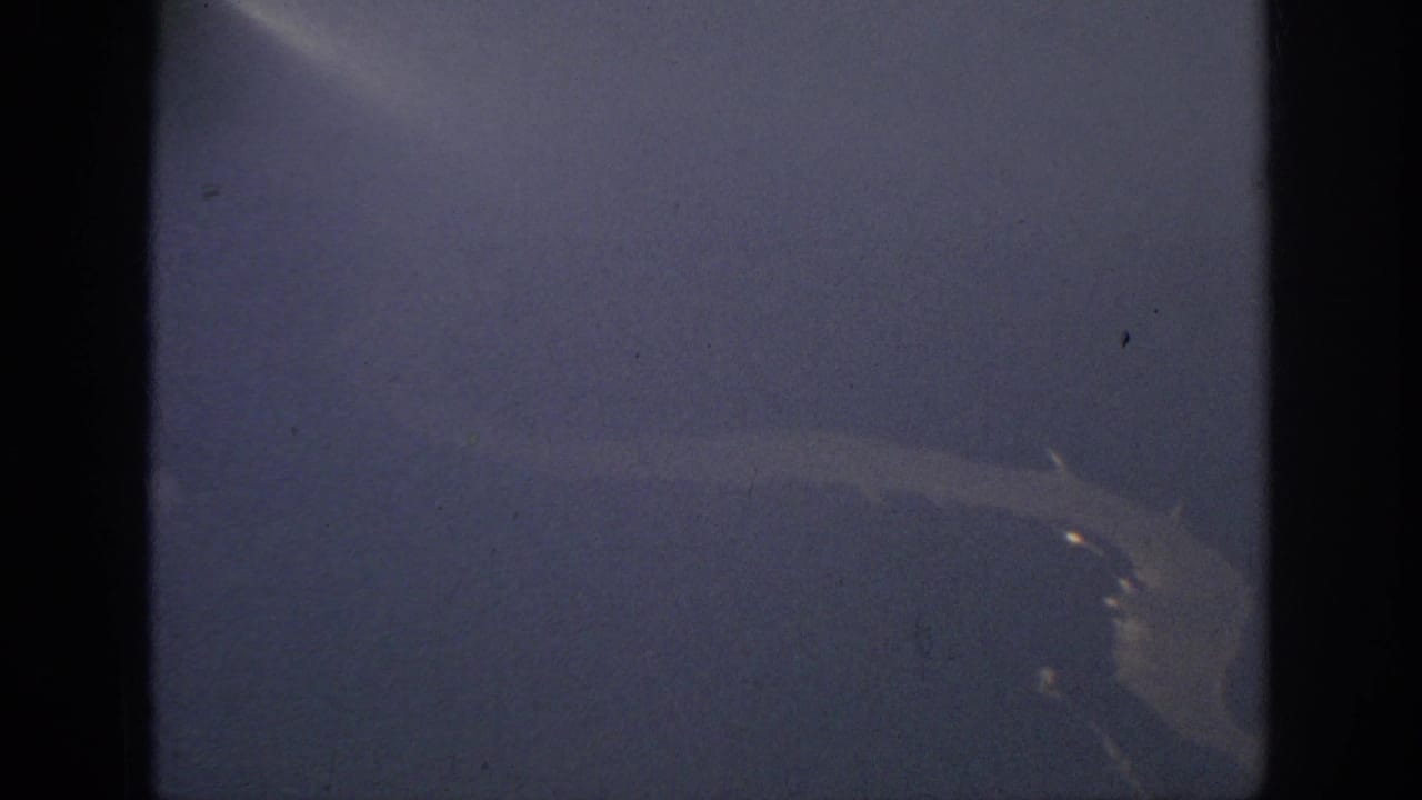 1962 Anaheim-area home-movie frame showing a distant pale river shape beneath a hazy blue-purple airplane view.
