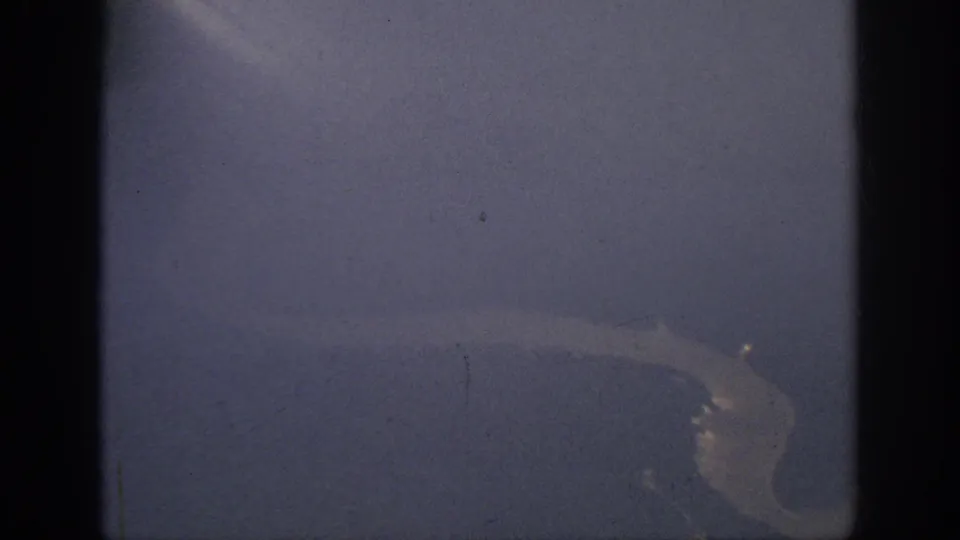 1962 home-movie aerial frame with a muted river bend below, dark gate borders, and visible dust and scratches.