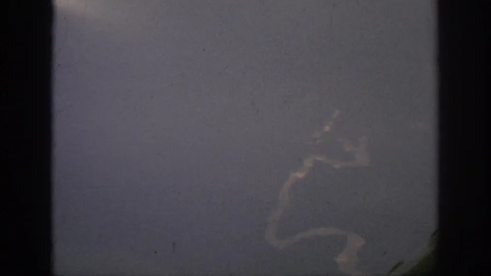 Grainy 1962 Anaheim-area aircraft view showing a pale winding water edge, window border and faint white streak near the lower right.