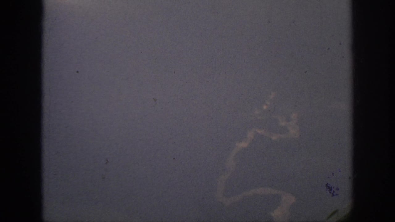 1962 home-movie frame showing a dim passenger-window view with clouds outside and dark window framing in the foreground.