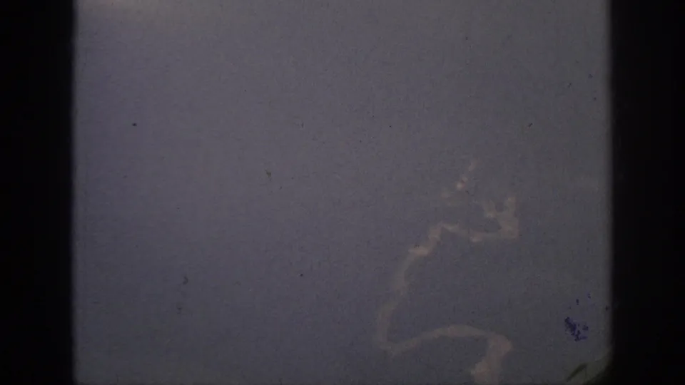 1962 home-movie frame showing a dim passenger-window view with clouds outside and dark window framing in the foreground.